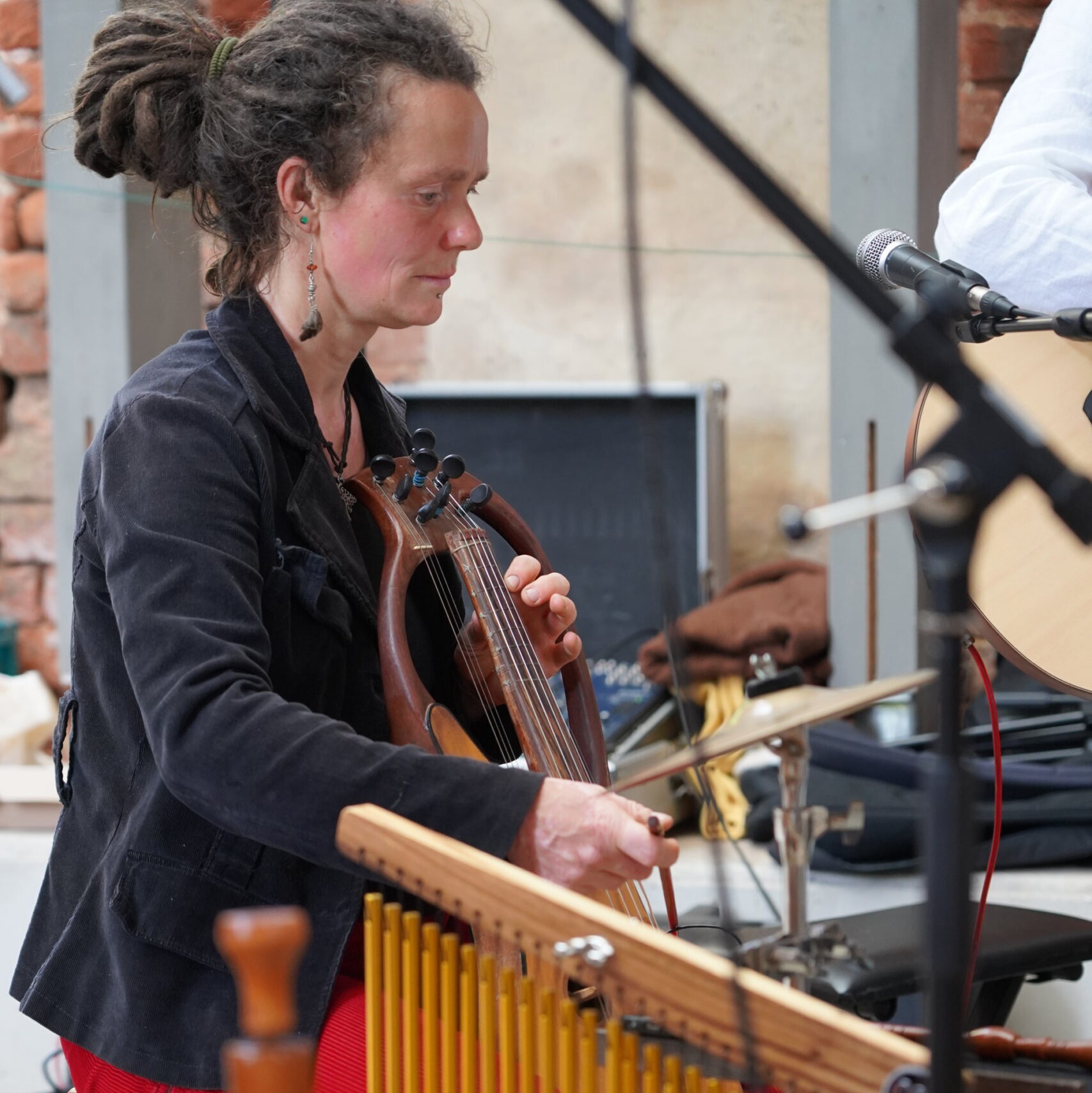 Silvia „Liese“ Needon musiziert auf ihrer Fidel. Zahlreiche Perkussionsinstrumente sowie technisches Equipment umgeben sie.
